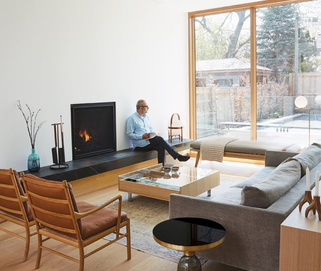 Living room space with couch and chairs facing a fireplace with a person sitting on the bench