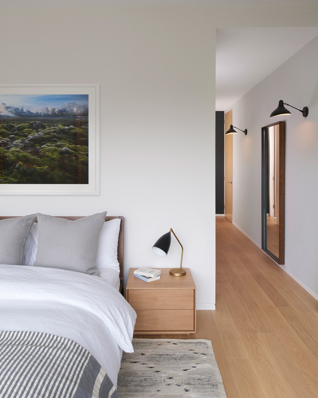 Bedroom design with a bedroom and a night stand on a wood floor. Wall sconces are visible along the walls. Leaside House by Arriz + Co and Altius Architecture  