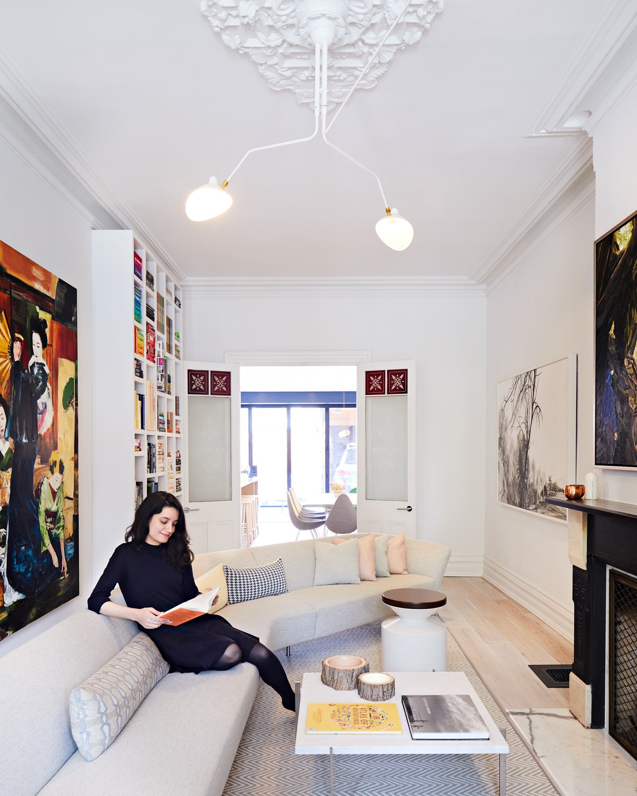Young lady seating on a living room sofa reading a book. Arts is filling the walls