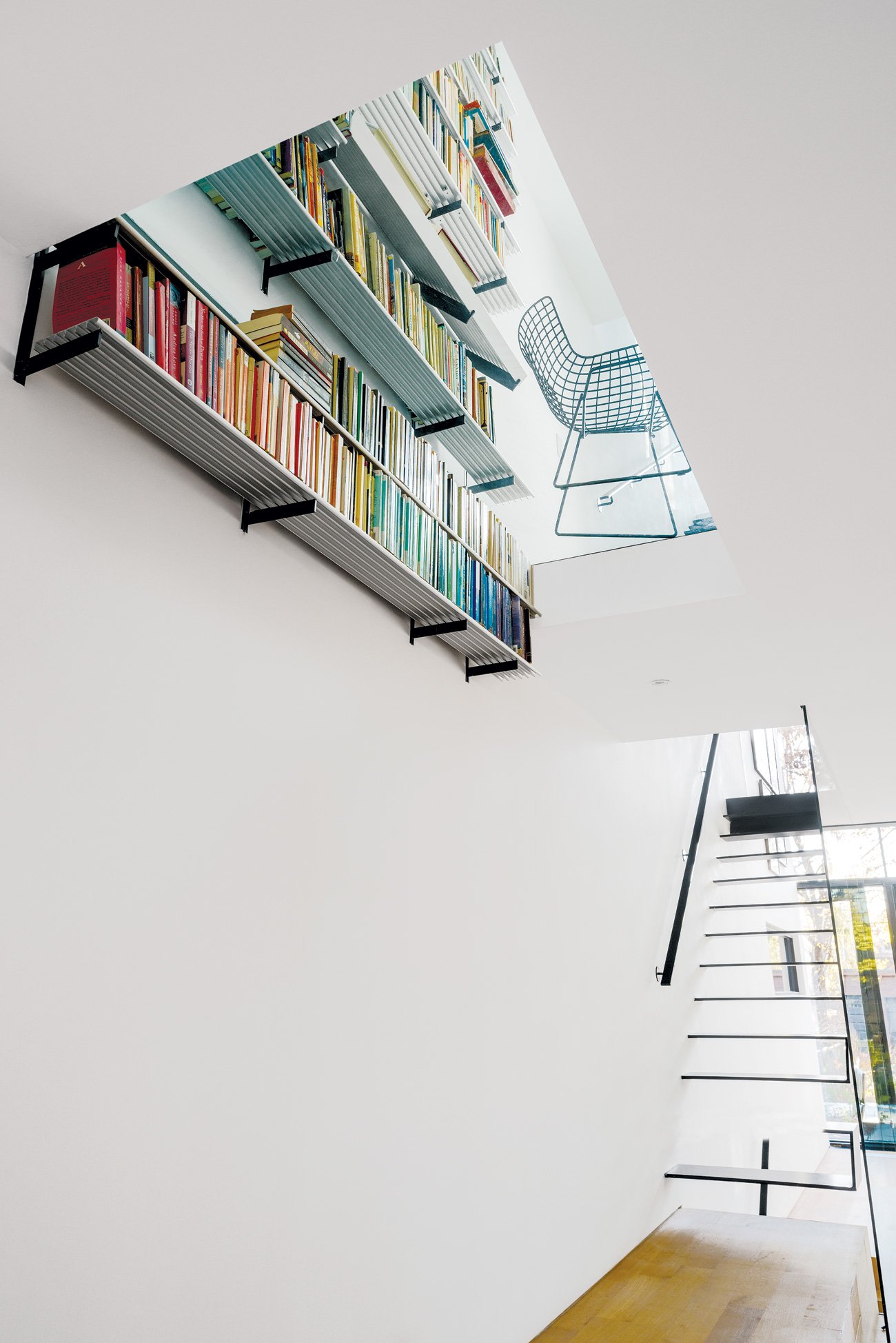 Home Library Ideas with designer Johnson Chou’s aluminum bookshelves appearing to pass through a glass floor.