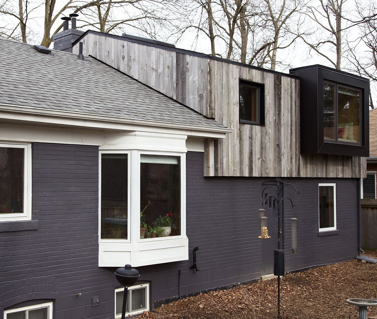 Backyard exterior view of a cabin-inspired bungalow addition in Mississauga with a pitched roof and reclaimed barnboard siding by Design Architecture Everyday 
